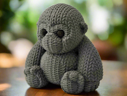 A hand-knitted gray gorilla sculpture placed on a wooden surface with a blurred background.