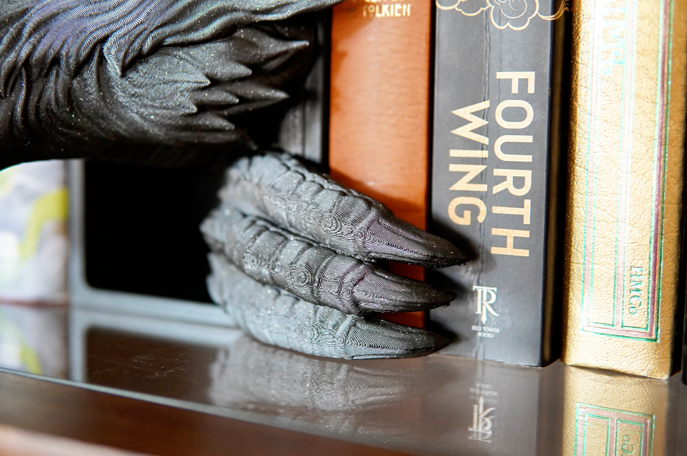  claw holding a book titled 'Fourth Wing' on a reflective surface.